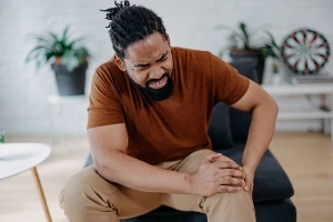 30-ish black man sitting and wincing in pain while holding his knee