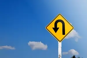 Up close image of a yellow left U-Turn sign against a blue sky